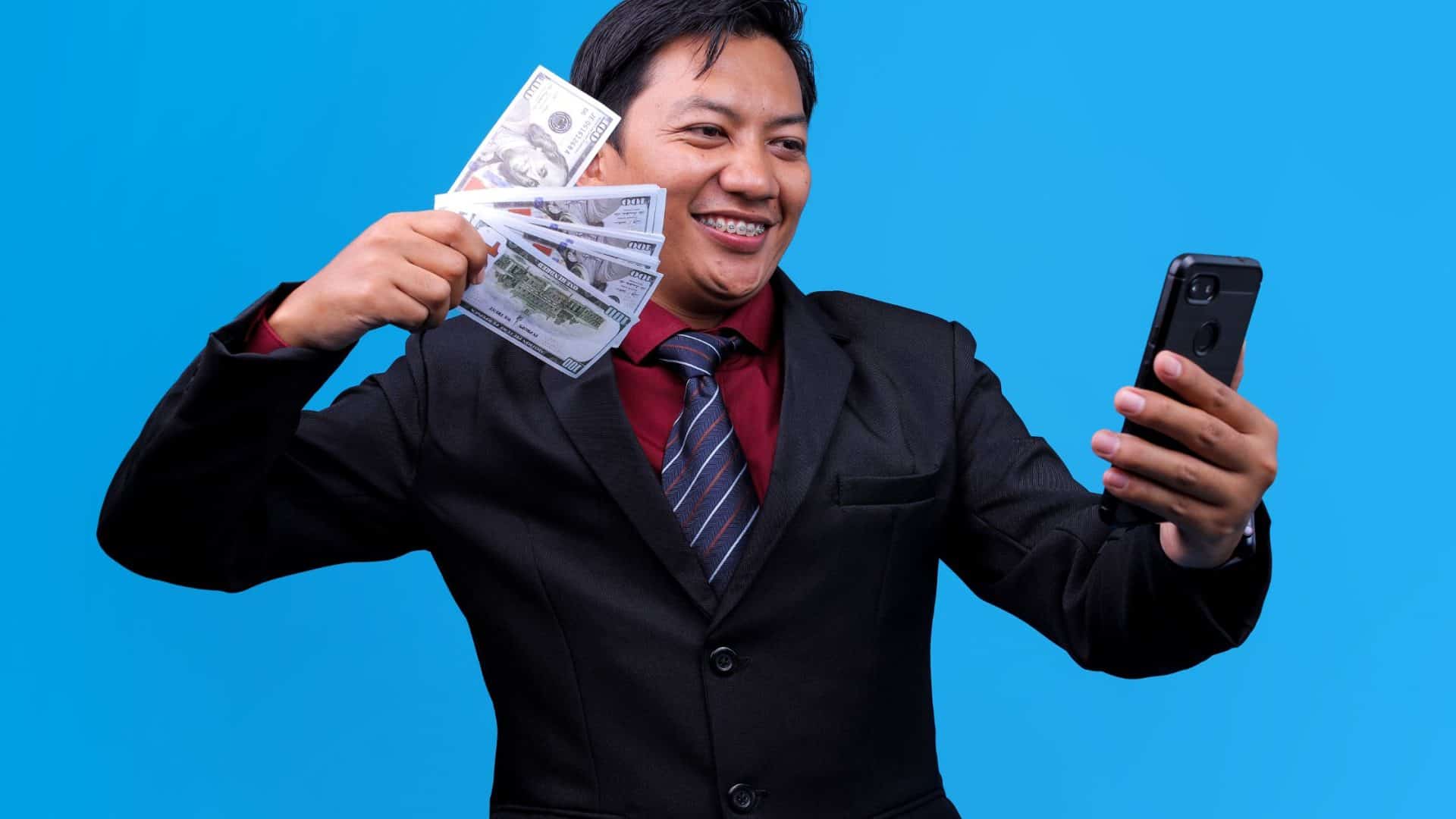 Faire payer vos clients plus vite. Homme avec de l'argent dans une main et un téléphone mobile dans l'autre sur fond bleu