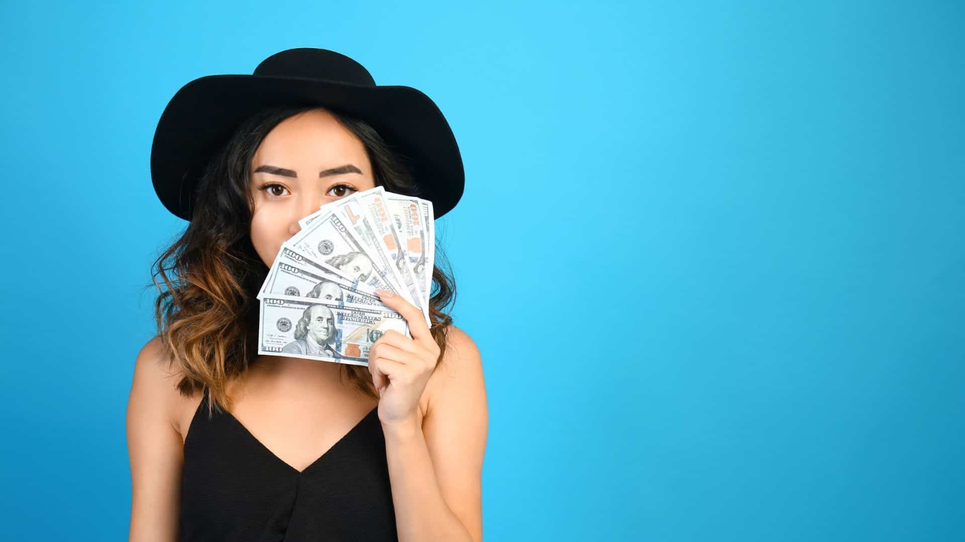 garder ses clients quand on augmente ses prix. Une femme avec un chapeau noir tenant de l'argent devant son visage